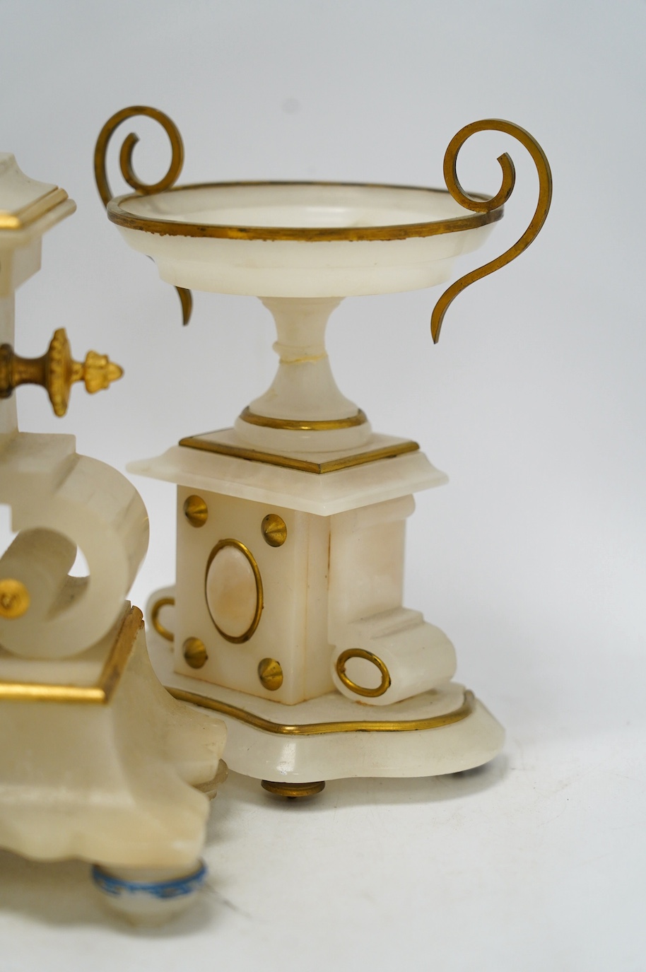 An early 20th century alabaster and gilt metal clock garniture with enamel panels, surmounted with a lion, with pendulum, no key, clock 30cm high. Condition - poor